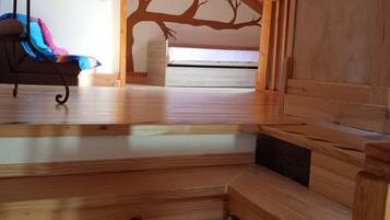 A room with a sloped ceiling, wooden beams, a bed, a chair, and a wall mural.