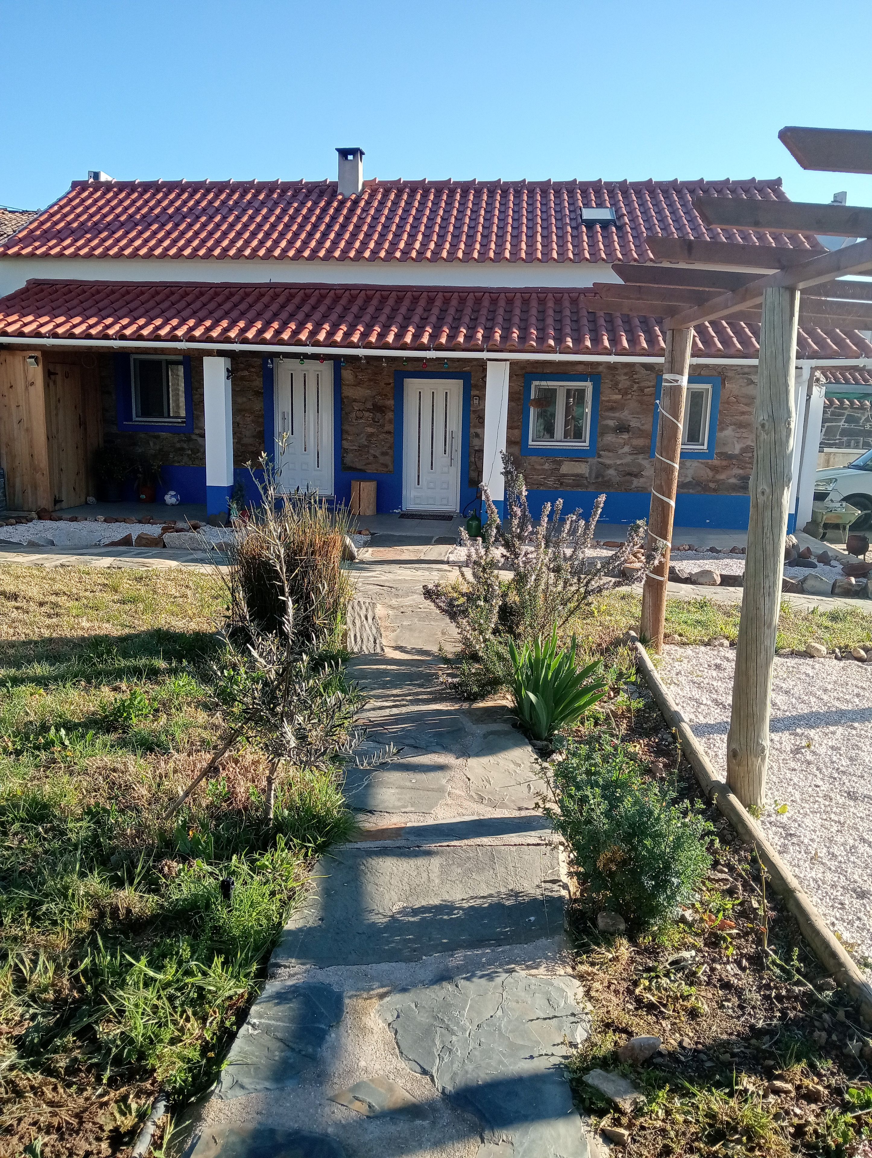 Ein Haus mit rotem Ziegeldach, Steinmauern und einer Veranda mit blauen Fensterrahmen.