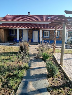 A house with a red-tiled roof, stone walls, and a front porch with blue-framed windows.
