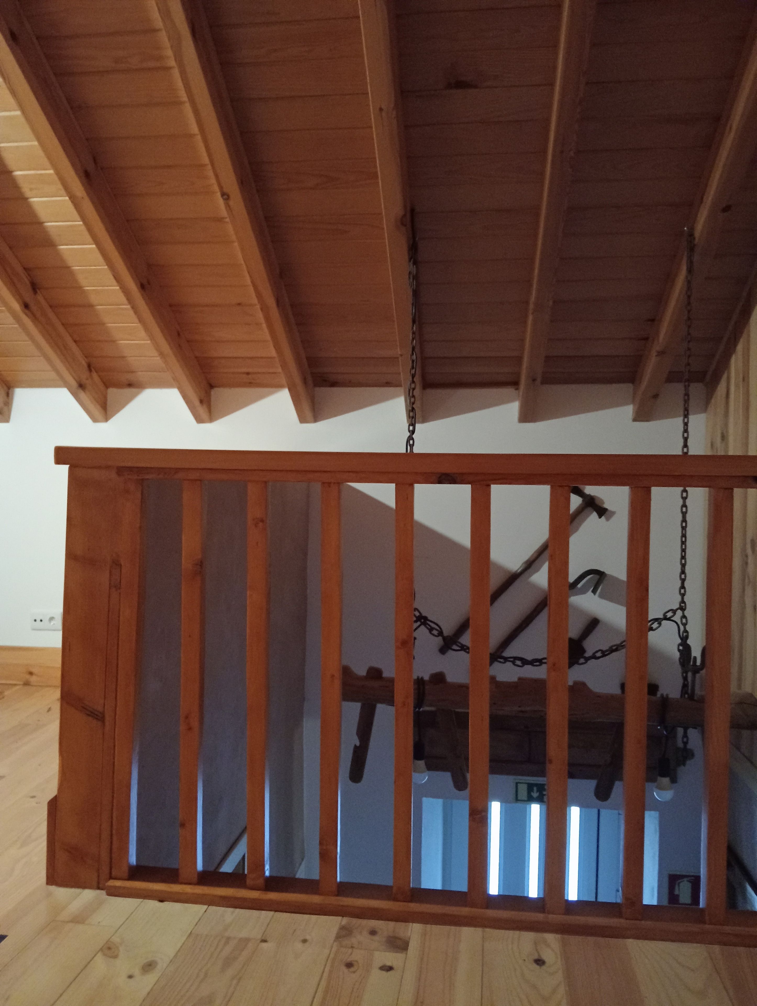 Ein Holzbalkon mit einem Metallgeländer, gestützt von Holzbalken und Ketten.