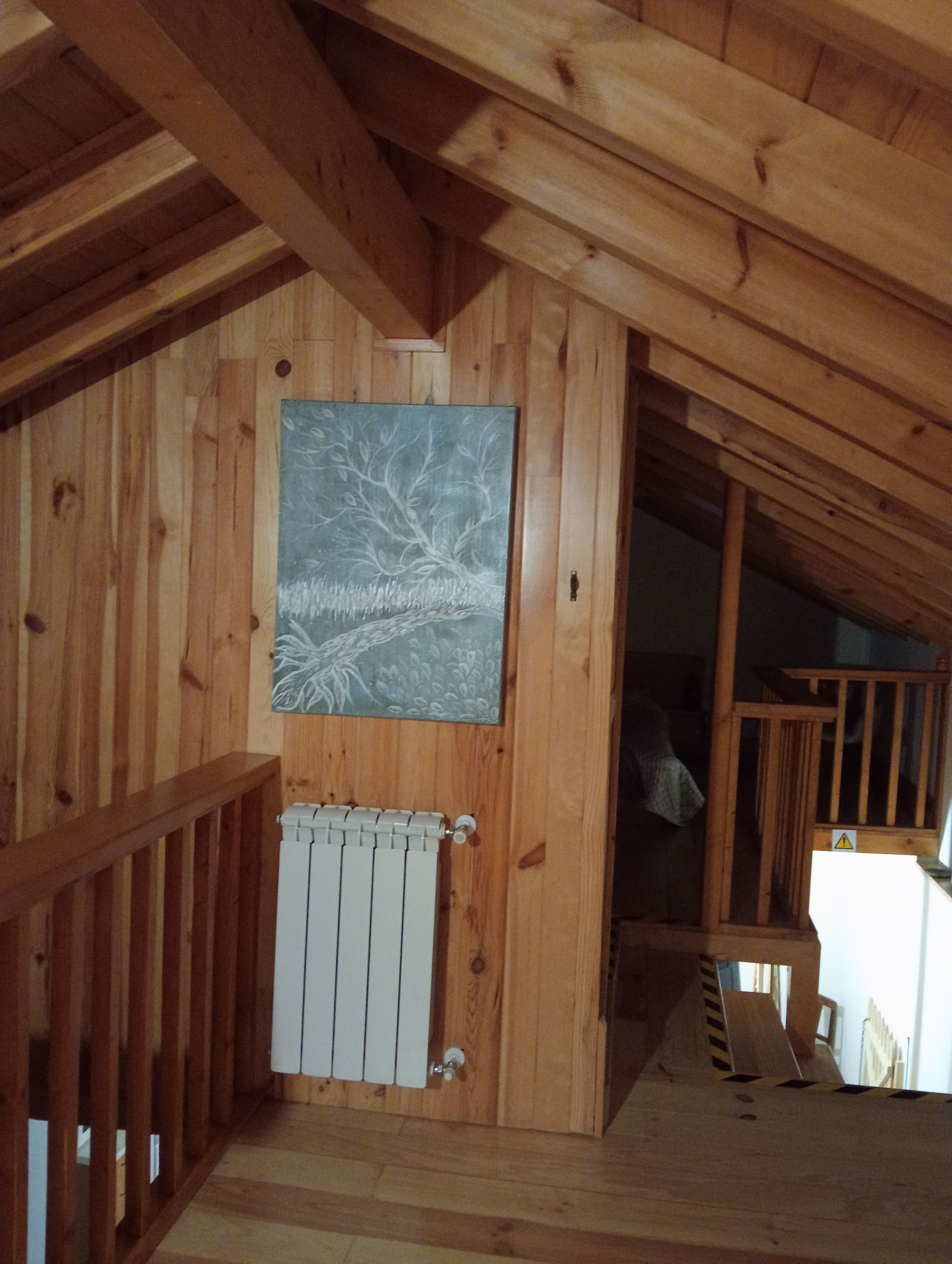 A wooden interior with a radiator, a wooden staircase, and a wall-mounted artwork.