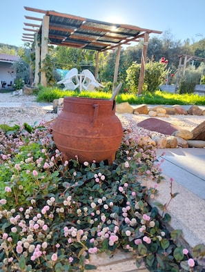 Ein Garten mit einem großen Metalltopf, einer Pergola und verschiedenen Pflanzen.