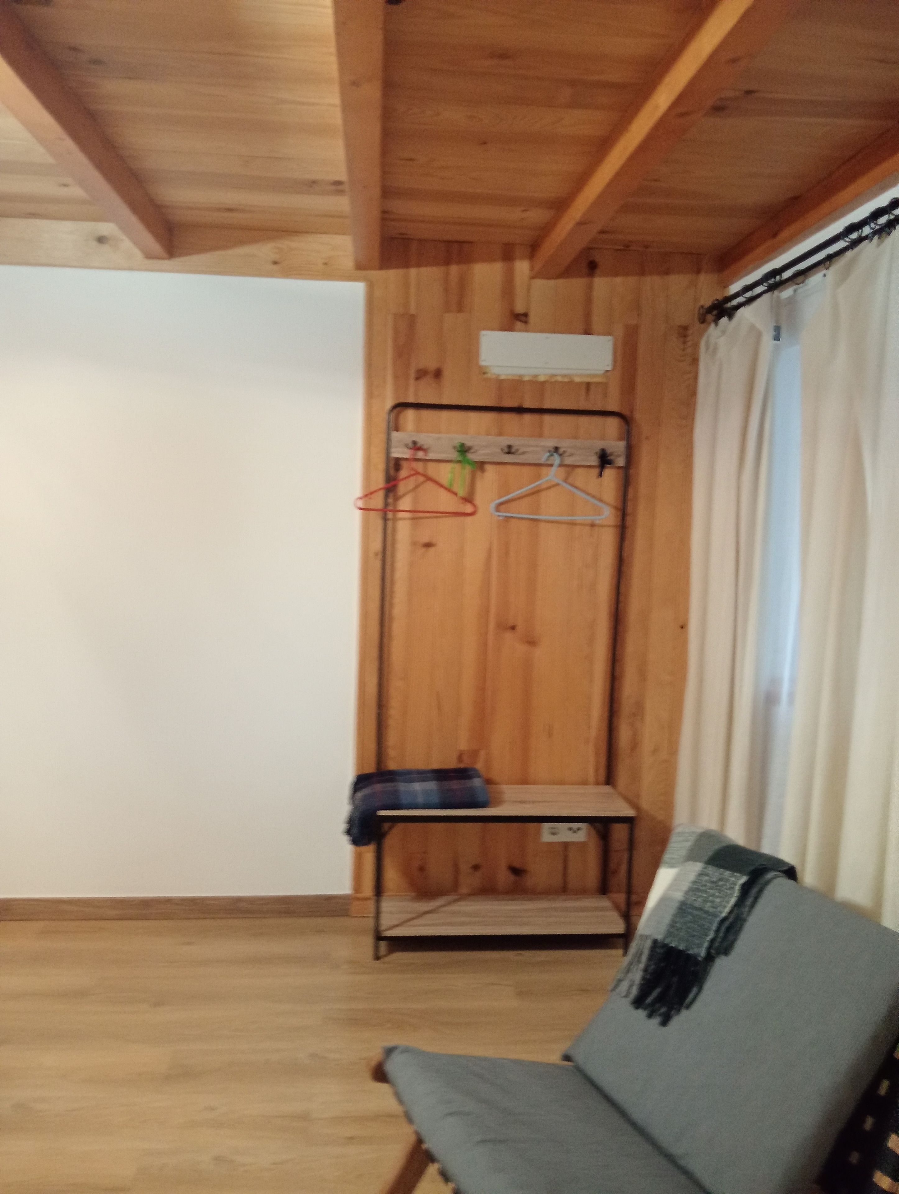 A room with a wooden ceiling, a bench, a coat rack with hangers, and a curtain.