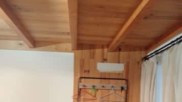 A room with a wooden ceiling, a bench, a coat rack with hangers, and a curtain.