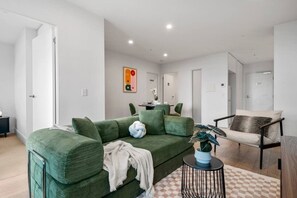 A modern living room with a green sofa, a small round table with a plant, and a chair with a cushion. - City View 3 Bedroom with Pool (Melbourne)