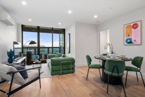 A modern living space with a balcony, a dining area with green chairs, and a city view. - City View 3 Bedroom with Pool (Melbourne)