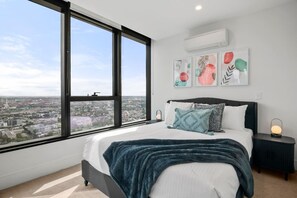 A bedroom with a large window, a bed with a blue blanket, and a city view. - City View 3 Bedroom with Pool (Melbourne)