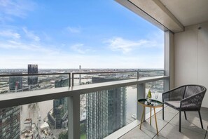 A balcony with a view of a cityscape, a chair, and a small table with a bottle and glass. - Sub Penthouse with Parking (Docklands)