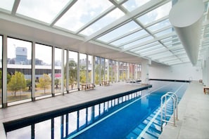An indoor swimming pool with clear glass ceilings, a long poolside area, and a view of the cityscape. - Central Apartment with Tennis (Southbank)