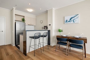 A modern kitchen with a central island, bar stools, a dining table with chairs, and a wall-mounted clock. - Central Apartment with Tennis (Southbank)