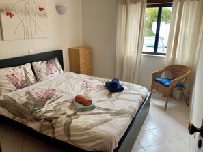 A hotel room with a bed, a chair, a wooden cabinet, and a window with curtains. - Sea View Dream | Ocean Views, Steps from the Beach, Lagos Algarve (Lagos)