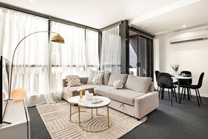 A modern living room with a sofa, a round coffee table, and a dining area with chairs. - Light-filled City 2 Bedroom (Melbourne)