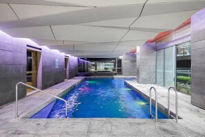 Ein Hallenbad mit glasklarer Wasseroberfläche, umgeben von Wänden mit einem geometrischen Muster und einem Glasbereich an einem Ende.