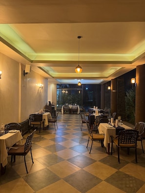 Un restaurante con suelo de cuadros, mesas dispuestas para comer y luminarias colgantes.