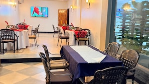 A hotel dining area with tables set for four, chairs, and a television screen. - NEXUS RESORTS HOTEL (Kampala)