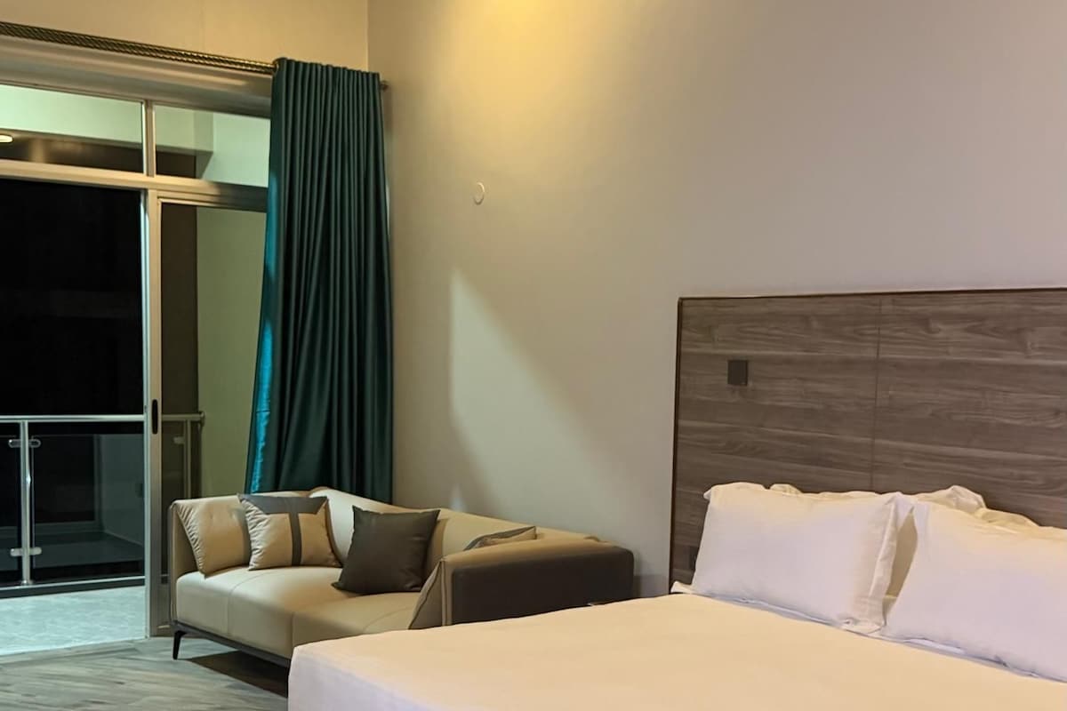 Habitació d'hotel amb un llit gran, un sofà i una porta corredissa de vidre que dona a un balcó.