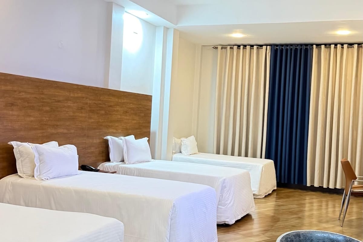 Habitació d'hotel amb dos llits, un panell de fusta al capçal, una cadira i un finestral gran amb cortines.