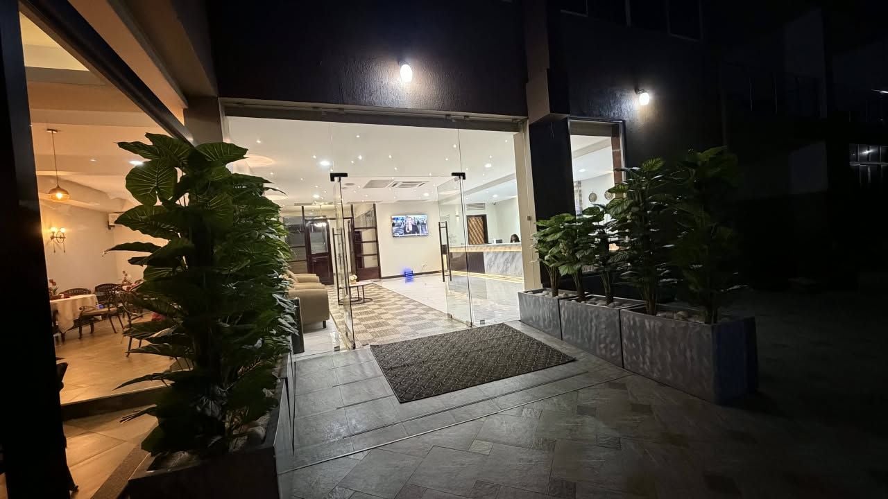 A hotel entrance with a reception desk, a waiting area, and a glass door leading inside.