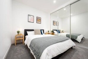 Una camera da letto moderna con un grande specchio, due letti, comodini e quadri appesi al muro.