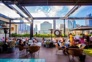 An outdoor seating area with tables and chairs, surrounded by potted plants and a city skyline view. - New York Style City 3 Bedroom (Melbourne)