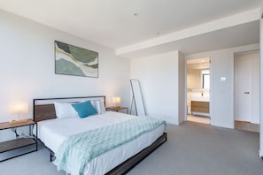 Une chambre moderne avec un grand lit, des tables de chevet, un tableau et une porte ouverte donnant sur une salle de bain.