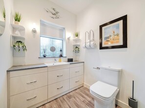 Een moderne badkamer met een witte wastafel, meubel en toilet. Er staan planten op de planken en hangt een lijst aan de muur.