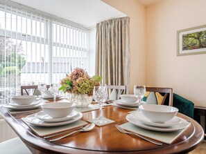 A dining room with a round table set for four, white plates, bowls, and cutlery, a vase with flowers, and a window with blinds. - Waltergarth (Settle)