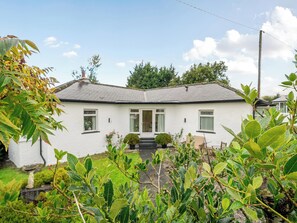 Een gelijkvloers huis met een witte gevel, een voortuin en een kleine tuin.