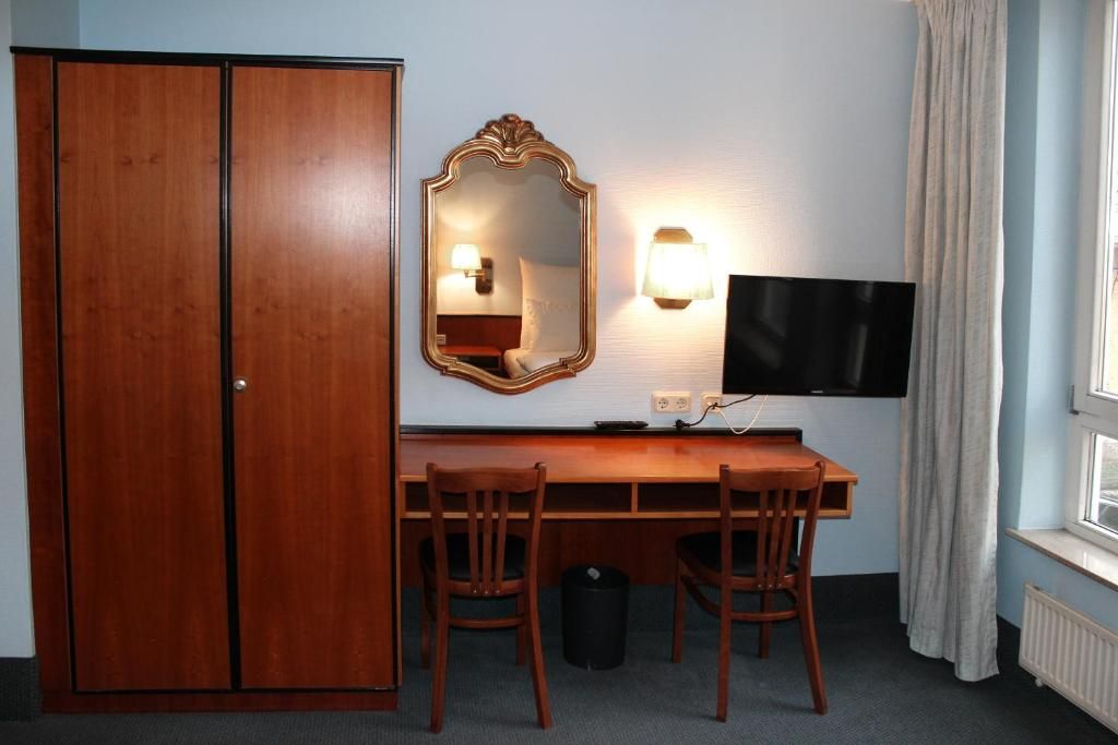 Una habitación de hotel con un escritorio de madera, dos sillas, un televisor, un espejo y un armario.