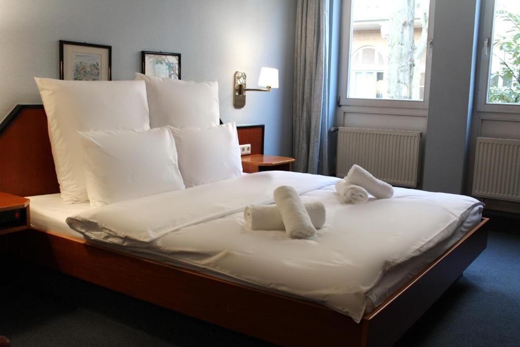 A hotel room with a large bed, two bedside tables, a wall-mounted lamp, and a window with curtains.