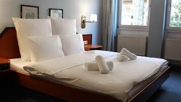 A hotel room with a large bed, two bedside tables, a wall-mounted lamp, and a window with curtains.