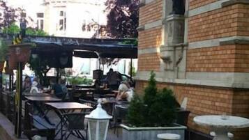 An outdoor seating area with tables and chairs, a white lantern, and a brick building with a statue.