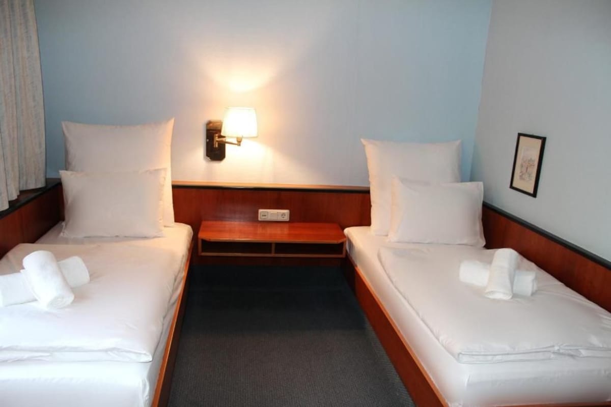 Een hotelkamer met twee eenpersoonsbedden, een nachtkastje, een wandlamp en een klein fotolijstje aan de muur.