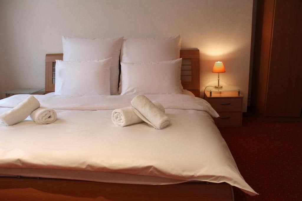A neatly made bed with pillows and rolled towels, a bedside lamp, and a wooden nightstand.