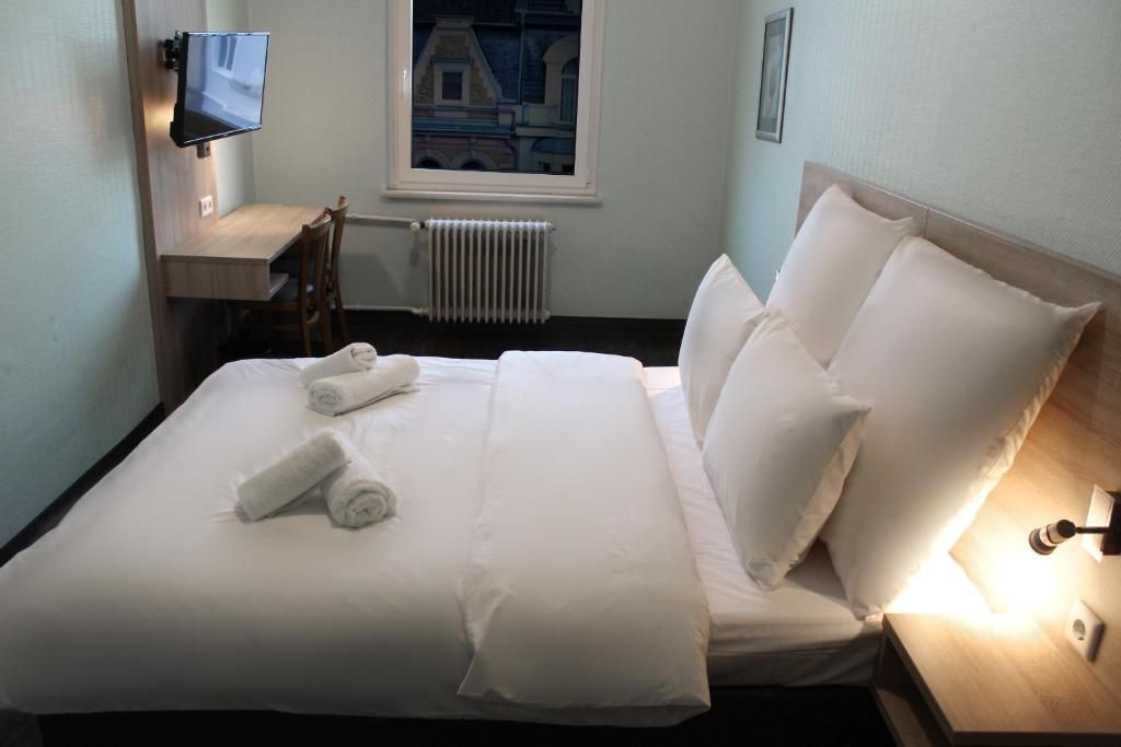 Una habitación de hotel con cama, televisión montada en la pared, ventana con vistas y mesita de noche con lámpara.