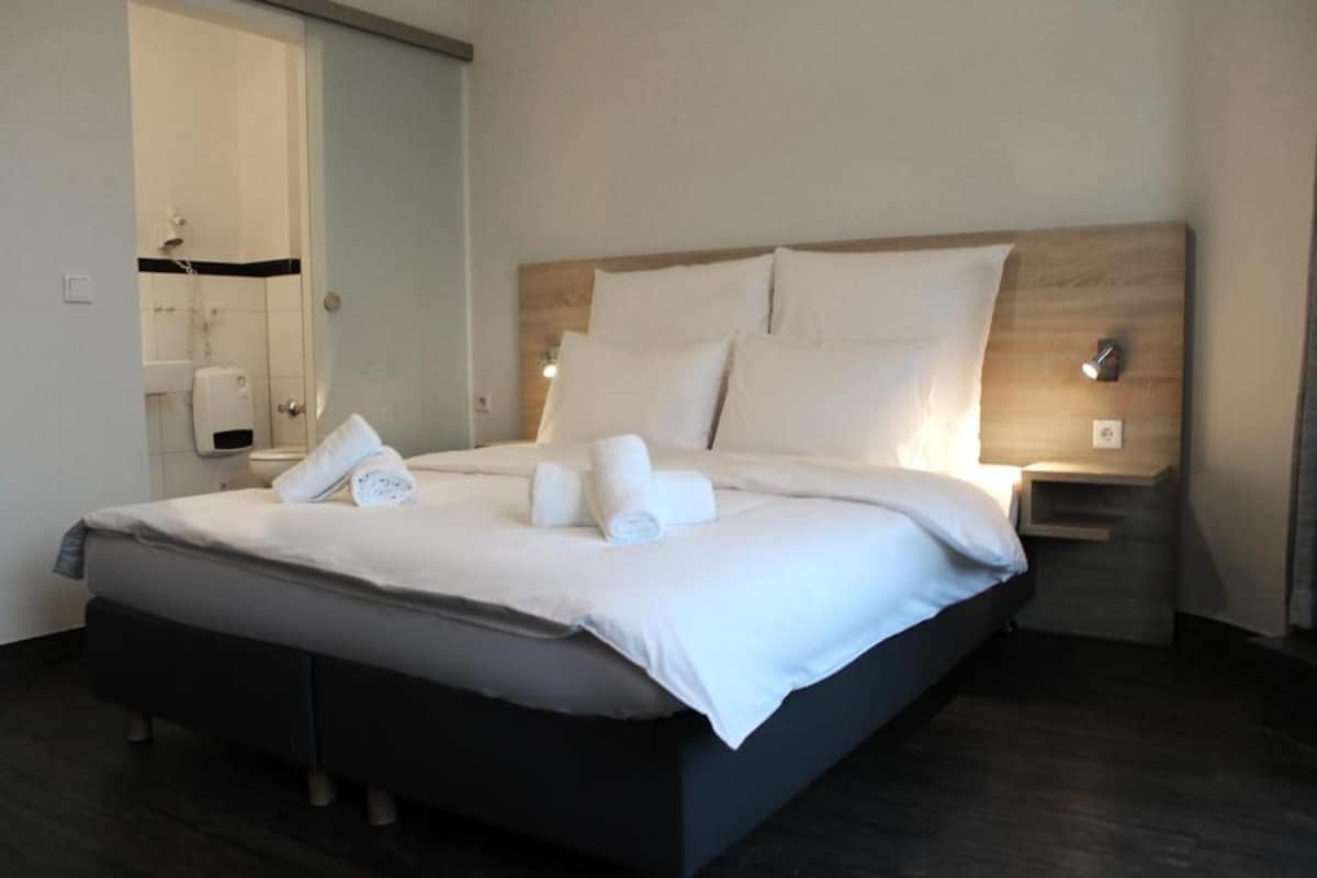 Een hotelkamer met een bed, nachtkastje en een badkamer zichtbaar door een open deur.