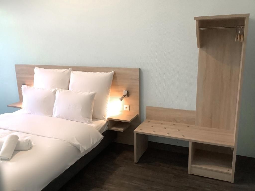 A hotel room with a bed, bedside table, and a wooden wardrobe.
