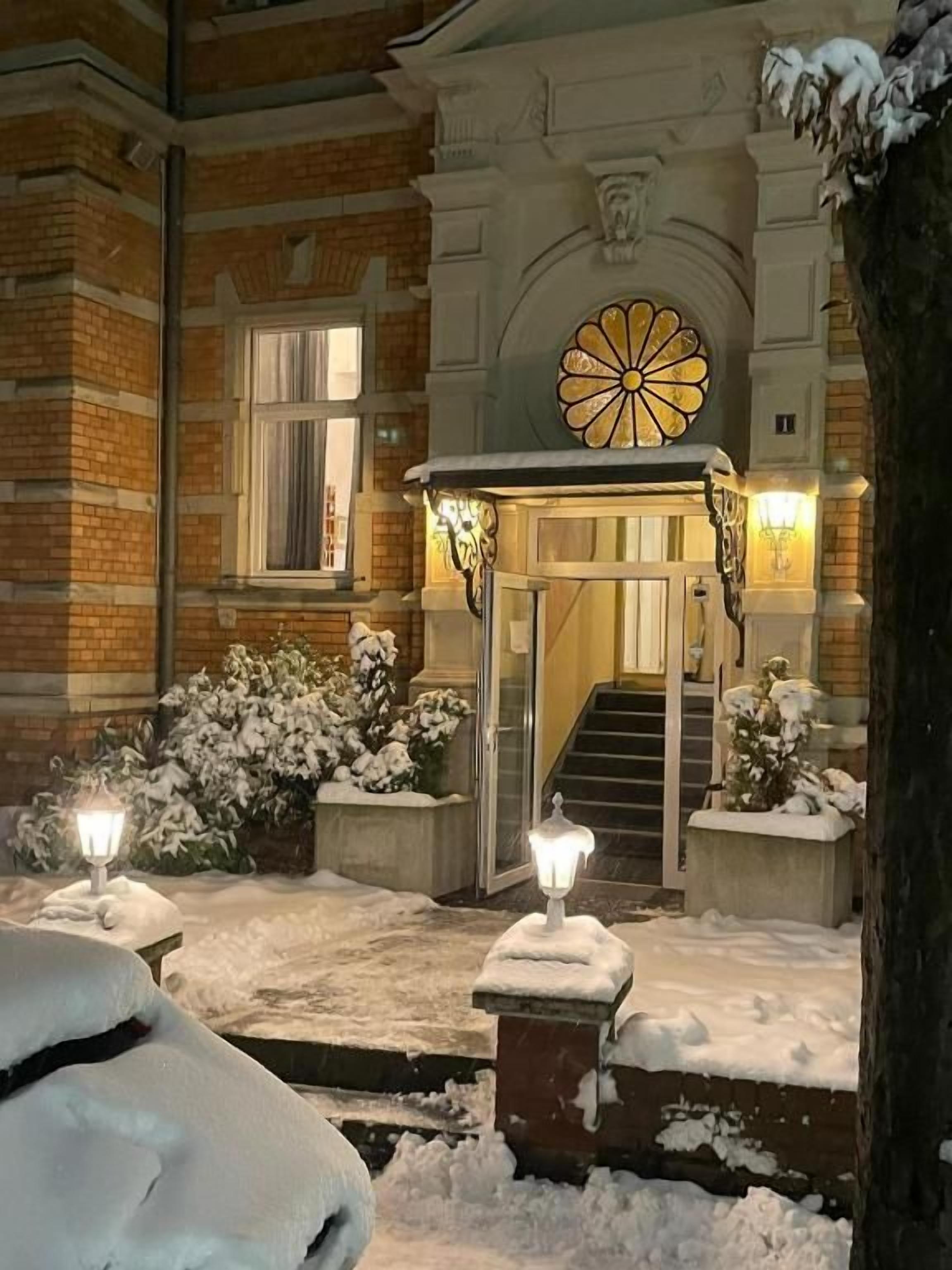 Entrada de hotel cubierta de nieve, con una escalera y un ventanal circular decorativo sobre la puerta.