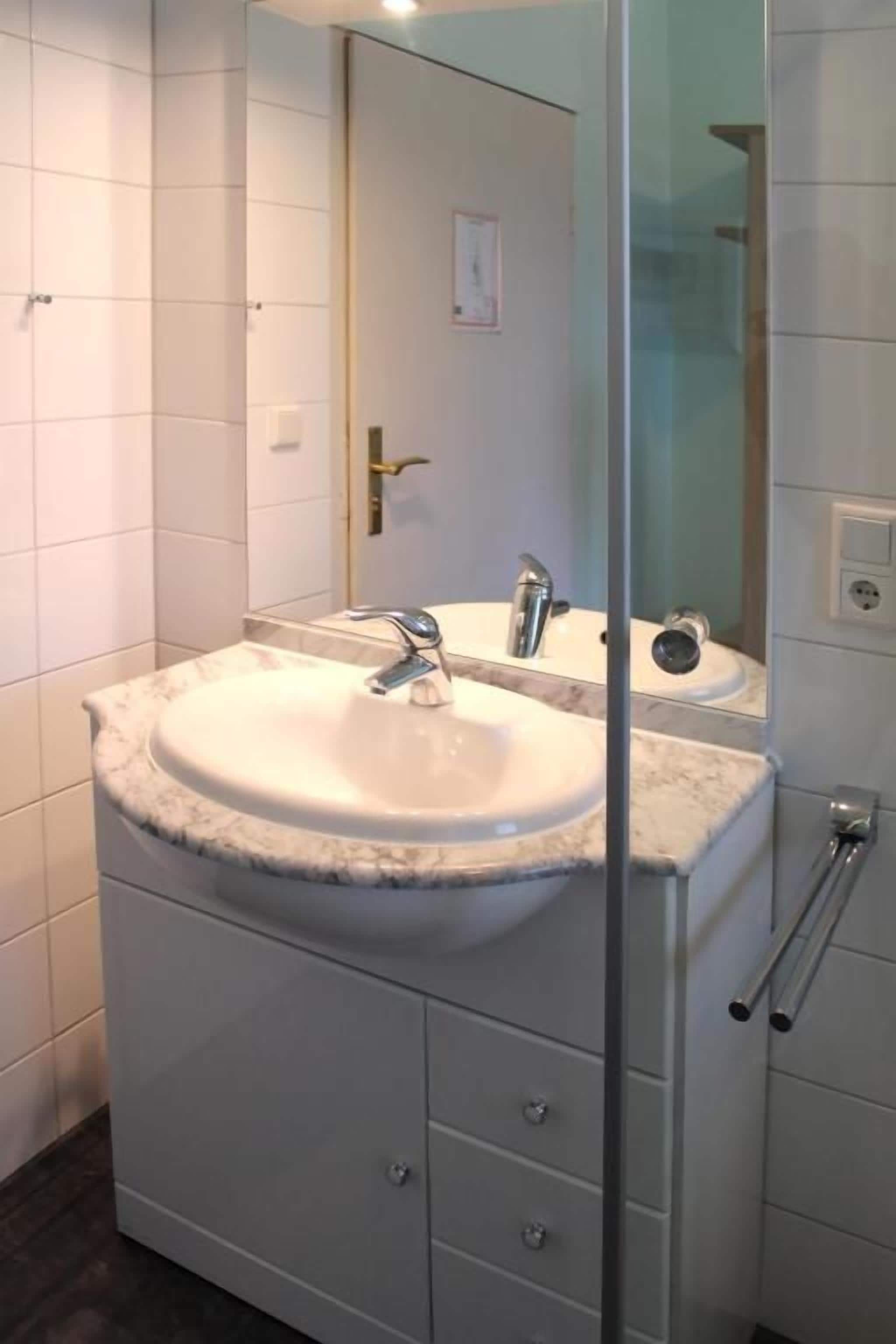 Une salle de bain avec un lavabo blanc, un miroir et une cabine de douche en verre.