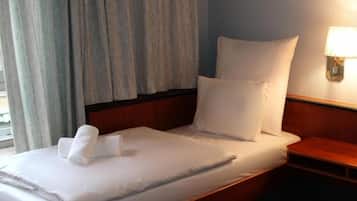 Habitación de hotel con una cama, una mesita de noche, una lámpara y un ventanal con cortinas.