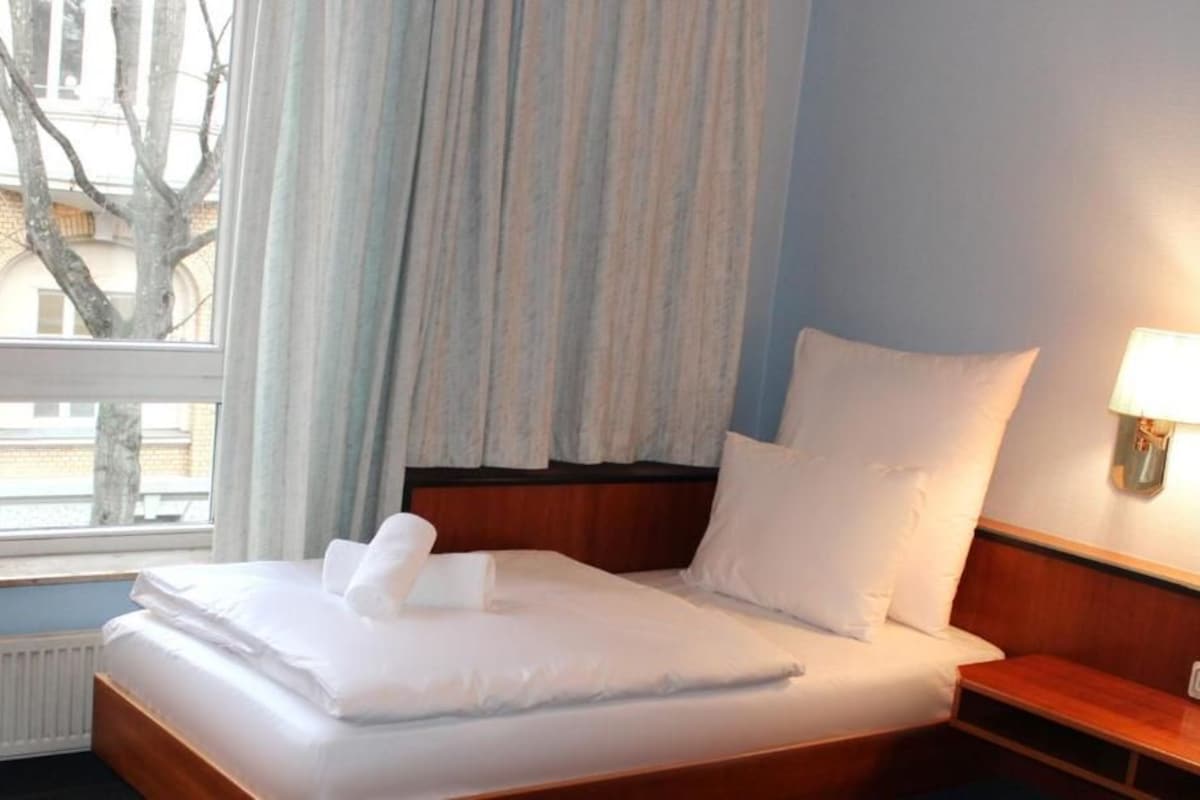 Een hotelkamer met een bed, nachtkastje, lamp en een raam met gordijnen.