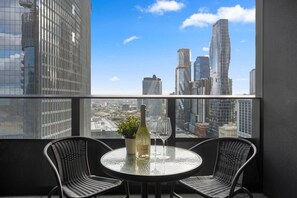 A balcony with a glass table, two wicker chairs, a bottle, and two wine glasses. - Elegant 2 Bedroom with Views (Docklands)