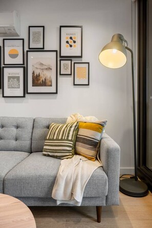 A grey sofa with striped and solid pillows, a framed artwork collection on the wall, and a floor lamp. - Elegant 2 Bedroom with Views (Docklands)