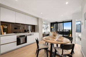 A modern kitchen with a dining area, featuring a central island, built-in appliances, and a view of the city. - Elegant 2 Bedroom with Views (Docklands)