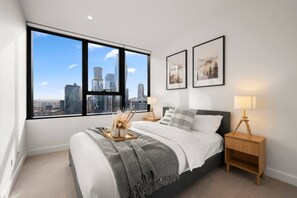 A bedroom with a large window, a bed, bedside tables, and framed pictures on the wall. - Elegant 2 Bedroom with Views (Docklands)