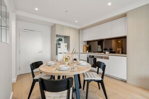 A modern kitchen with white cabinets, a dining area with a round table and chairs, and a visible door leading to another room. - Elegant 2 Bedroom with Views (Docklands)