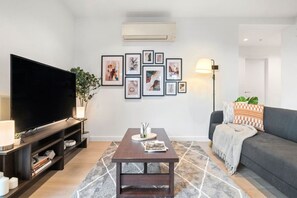 A living room with a flat-screen TV, a coffee table, a sofa, a patterned rug, and framed pictures on the wall. - Urban Treehouse Oasis (Docklands)