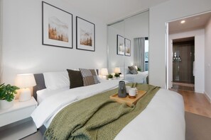 A modern hotel room with a large bed, bedside lamps, a green throw blanket, and a tray with a coffee pot and cups. - Scandi Oasis with Sky Views (Melbourne)