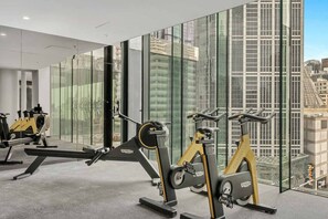 A gym with stationary bikes and a rowing machine, large windows, and a city view. - Scandi Oasis with Sky Views (Melbourne)