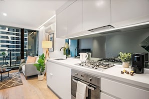 A modern kitchen with a gas stove, coffee machine, and a view of the city. - Stylish City 2 Bedroom Gem (Melbourne)